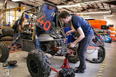 An Olin student works on a mini baja vehicle inside the large project building at Olin College