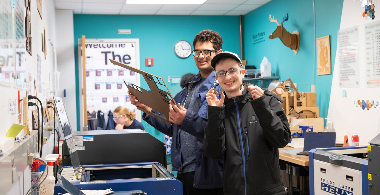 Two students hold up lazer cuts.