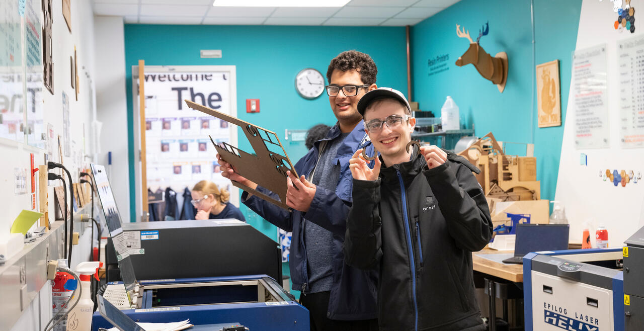 Two students holding up cutouts from shop machinery 